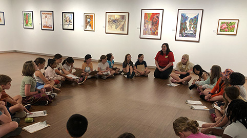 a group of children sitting in a circle in an art gallery