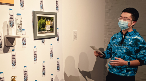 a man wearing a face mask stands in front of a wall of water bottles