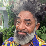 there is a man with a beard and a colorful shirt standing in front of a house
